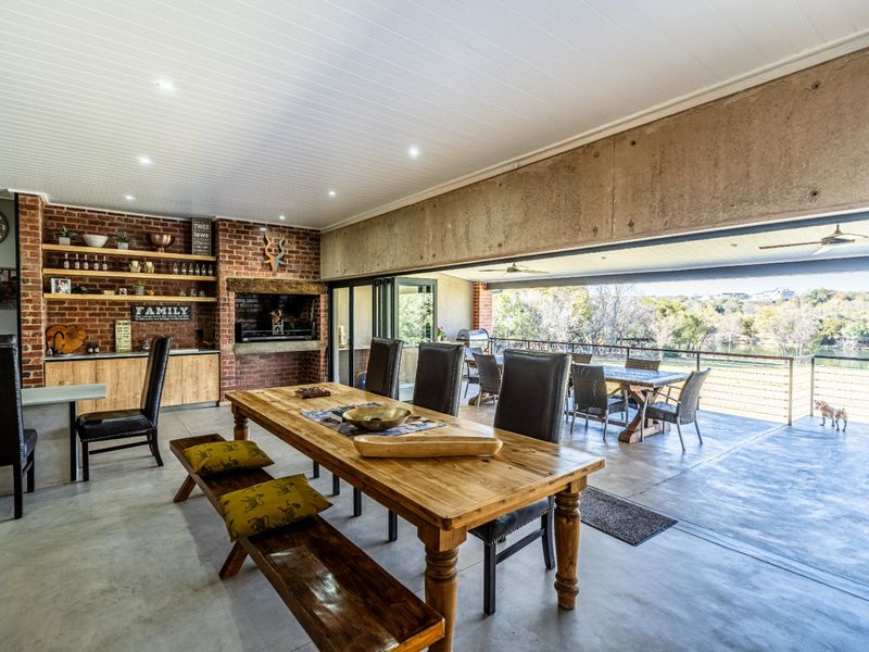 Spacious open-plan living and dining area featuring exposed brickwork, a built-in fireplace, polished concrete floors, and seamless flow to an outdoor patio.