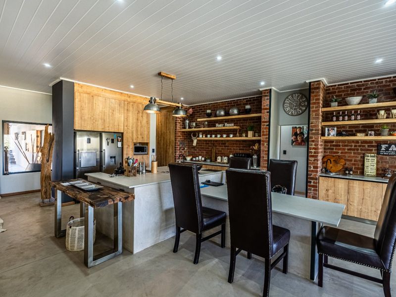 Modern open-plan kitchen featuring exposed brick walls, a large central island with stone countertops, custom timber cabinetry, and polished concrete flooring.
