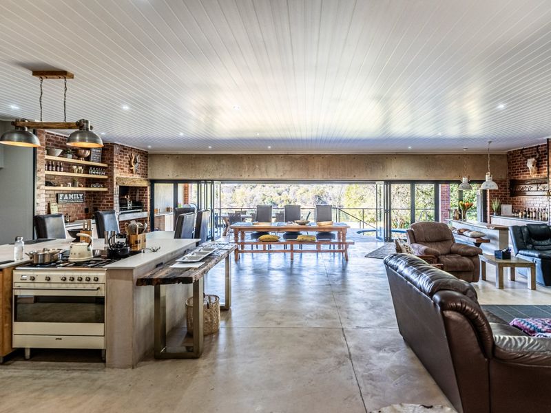 Spacious open-plan living area featuring polished concrete floors, exposed brick walls, a modern kitchen with island, and large stacking doors opening to the outdoors.