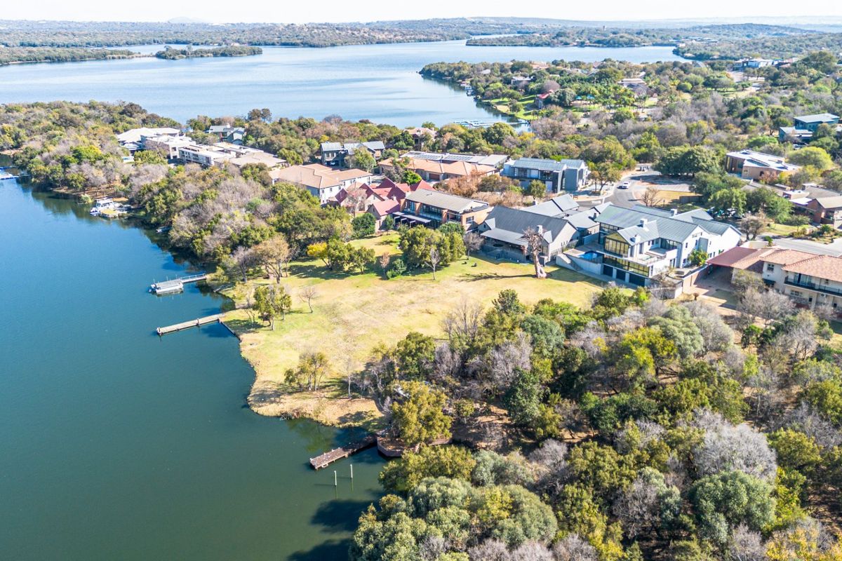 Aerial view of a waterfront residential estate featuring expansive green lawns, private jetty access, and scenic lake views.