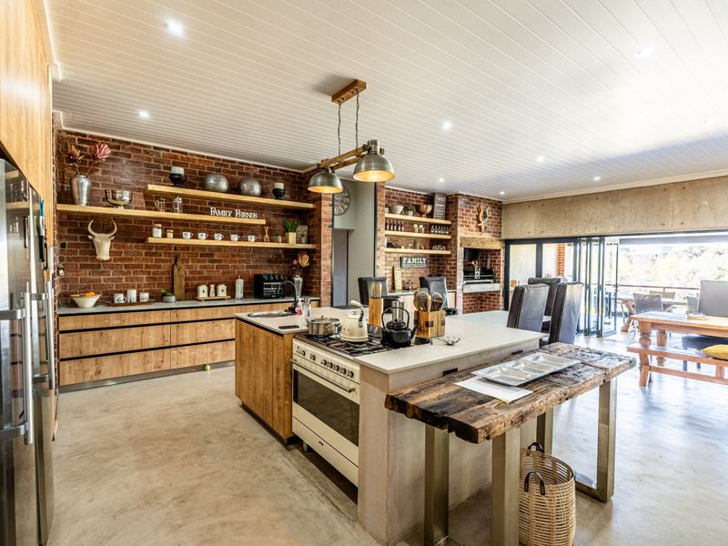 Spacious open-plan kitchen and living area featuring exposed brick walls, concrete floors, a large central island with gas stove, and seamless access to the patio.