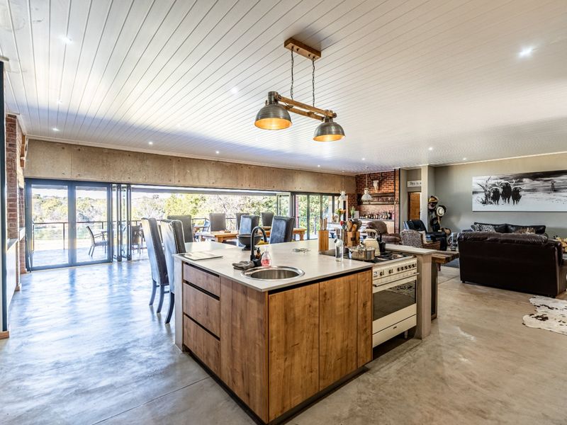 Spacious open-plan living area featuring a modern kitchen island, concrete floors, exposed brick accents, and large stacking doors opening to an outdoor patio.