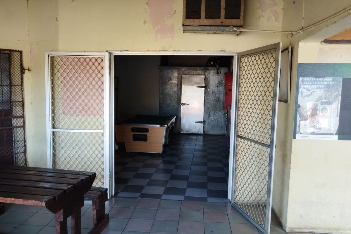 Commercial utility area featuring a walk-in cool room, tiled flooring, and security screen doors, showing signs of wear and peeling paint.