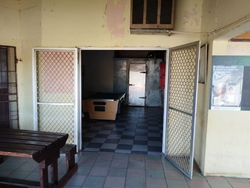 Commercial utility area featuring a walk-in cool room, tiled flooring, and security screen doors, showing signs of wear and peeling paint.