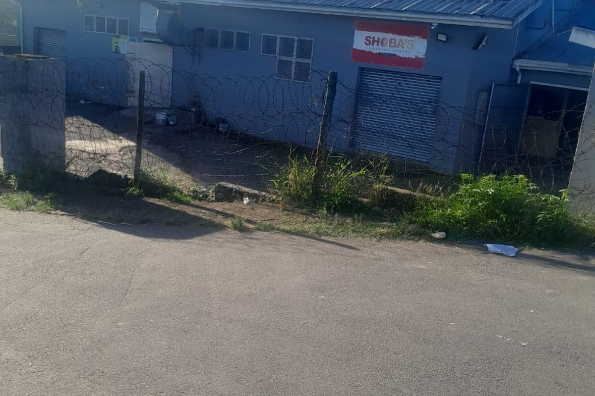 Rear view of a commercial building featuring metal roller shutter doors, corrugated roofing, and secured perimeter fencing with razor wire.