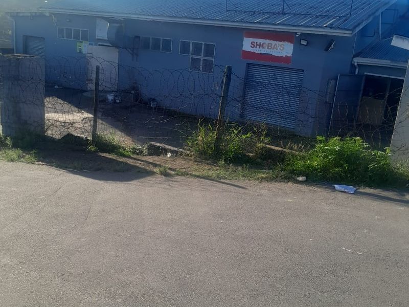 Rear view of a commercial building featuring metal roller shutter doors, corrugated roofing, and secured perimeter fencing with razor wire.
