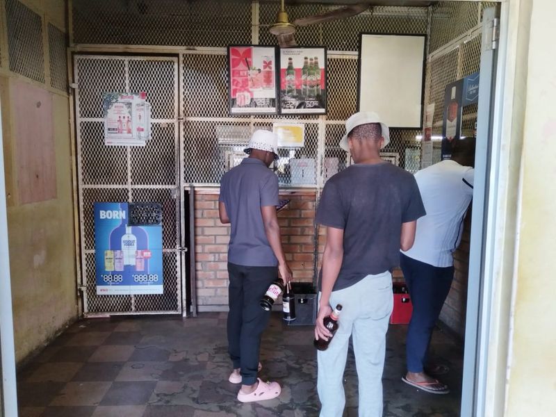 A commercial bar area featuring a security mesh partition, brick counter base, and tiled flooring, currently showing significant signs of wear and tear.