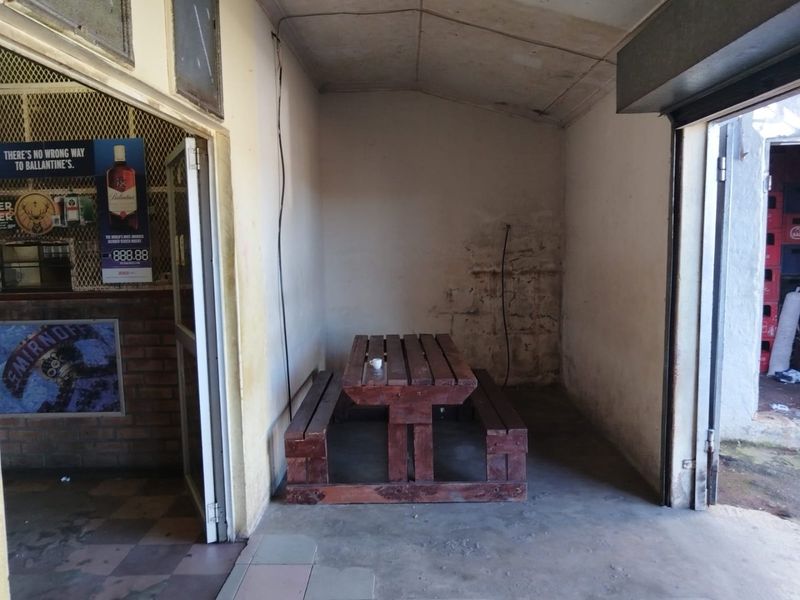 A covered outdoor seating area featuring concrete floors, exposed brickwork, and a roller shutter door, currently showing signs of wear and maintenance requirements.
