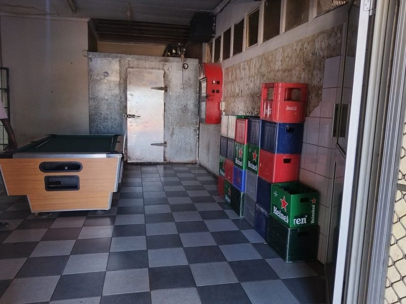 Utility area featuring a walk-in cold storage unit, tiled flooring, and wall tiling with visible plaster damage.