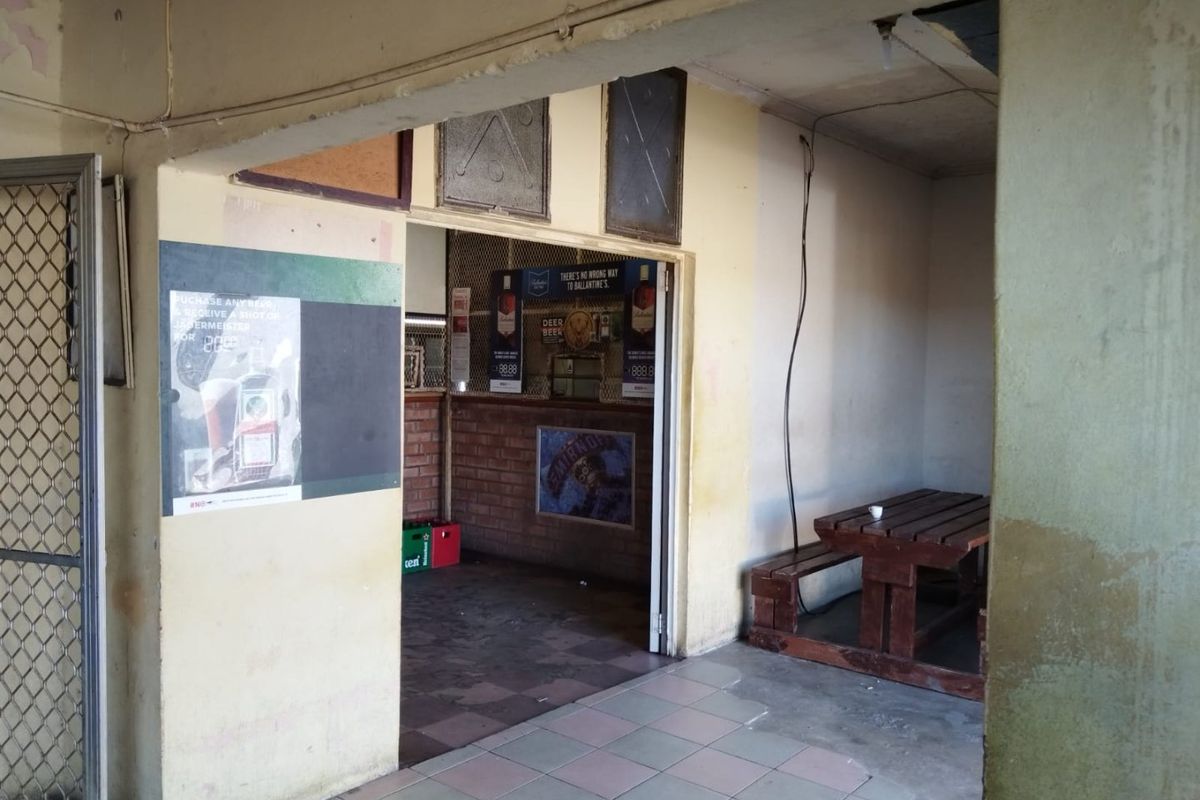 A commercial bar area featuring a service counter, brick wall accents, and tiled flooring, currently showing significant signs of wear and maintenance requirements.