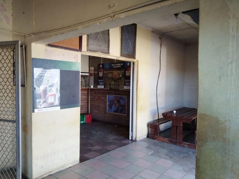 A commercial bar area featuring a service counter, brick wall accents, and tiled flooring, currently showing significant signs of wear and maintenance requirements.