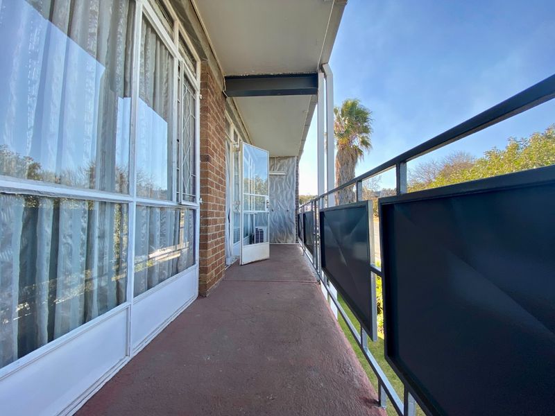 A covered balcony featuring a metal balustrade, brick exterior wall, and large sliding glass doors providing access to the apartment interior.