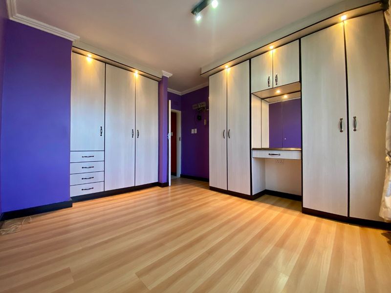 A spacious bedroom featuring extensive built-in cabinetry with an integrated vanity, laminate flooring, and modern recessed lighting.