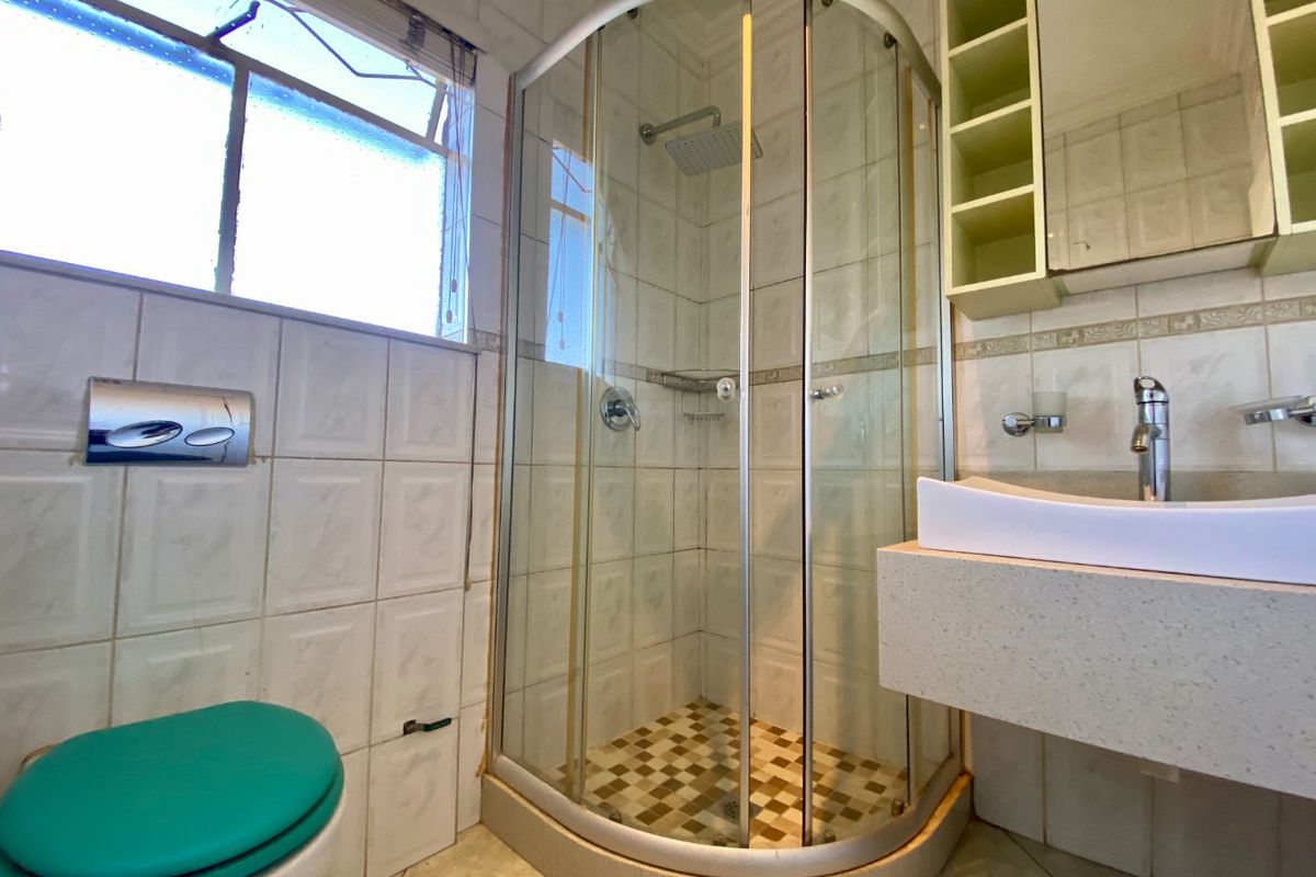 A functional bathroom featuring a corner shower enclosure, wall-mounted toilet, and a floating vanity with basin, finished with tiled walls and flooring.