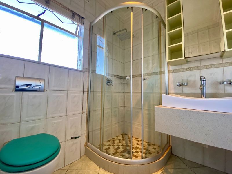 A functional bathroom featuring a corner shower enclosure, wall-mounted toilet, and a floating vanity with basin, finished with tiled walls and flooring.