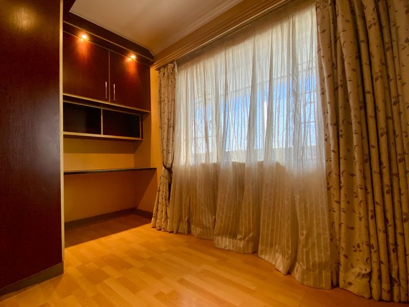 A bedroom featuring laminate flooring, built-in cabinetry with integrated lighting, and large windows with curtains and security bars.