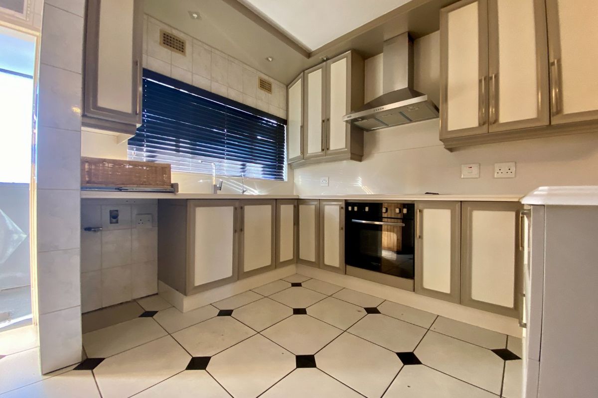 A functional kitchen featuring built-in cabinetry, a stainless steel extractor fan, a built-in oven, and tiled flooring with a classic pattern.