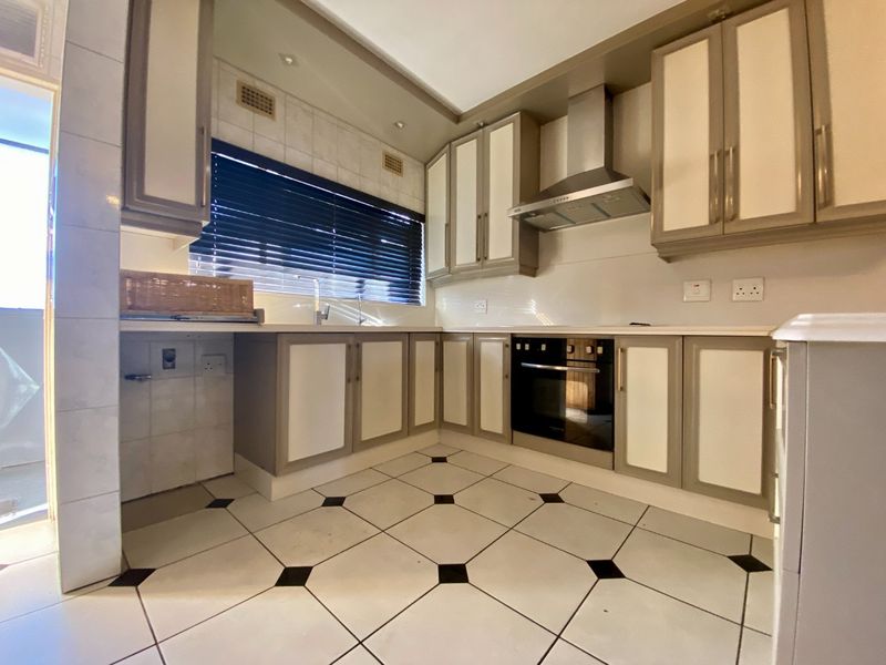 A functional kitchen featuring built-in cabinetry, a stainless steel extractor fan, a built-in oven, and tiled flooring with a classic pattern.