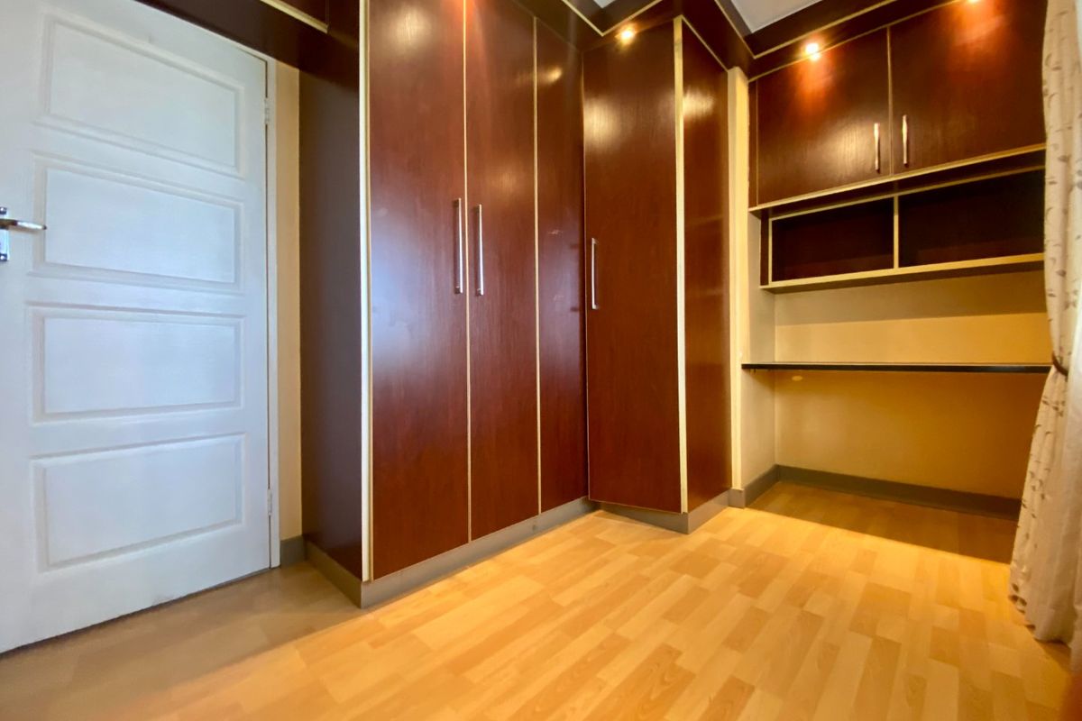 A bedroom featuring dark wood built-in cupboards, a matching built-in desk, recessed lighting, and light laminate flooring.