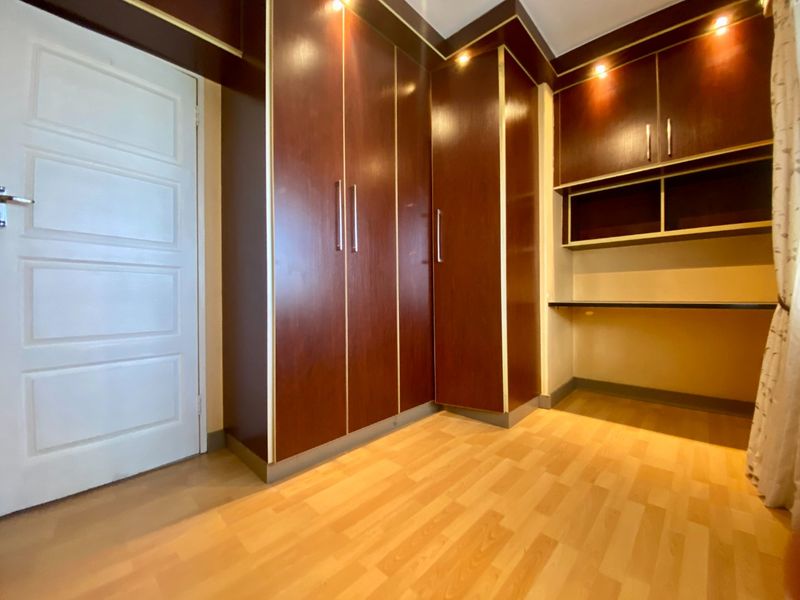 A bedroom featuring dark wood built-in cupboards, a matching built-in desk, recessed lighting, and light laminate flooring.