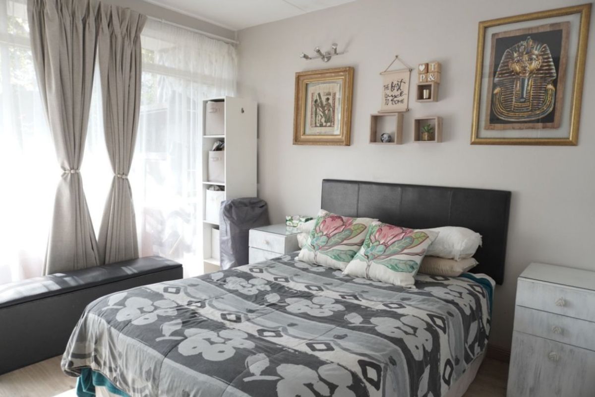 A well-lit bedroom featuring neutral wall tones, large windows with curtains, and a functional layout suitable for a comfortable sleeping space.