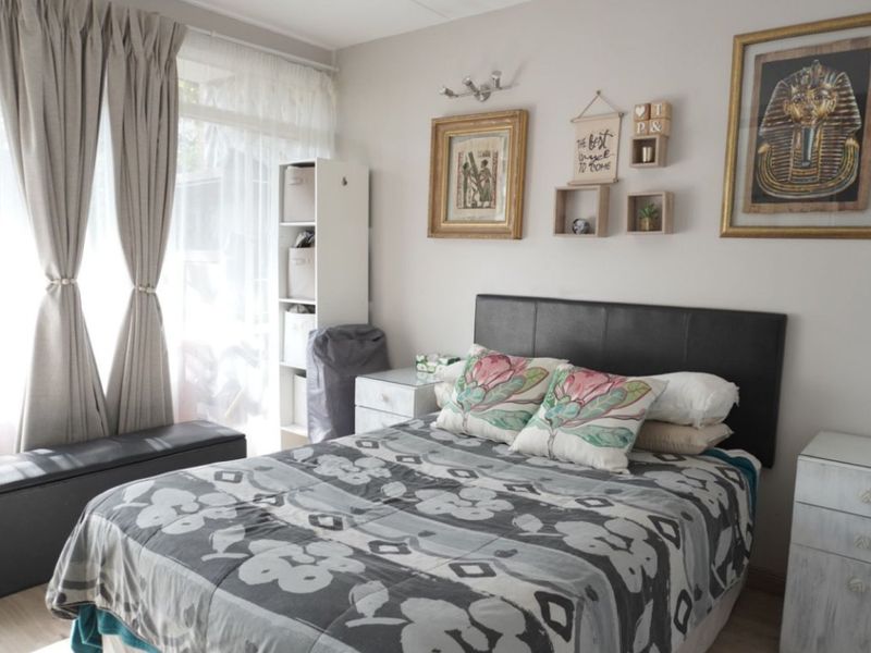 A well-lit bedroom featuring neutral wall tones, large windows with curtains, and a functional layout suitable for a comfortable sleeping space.