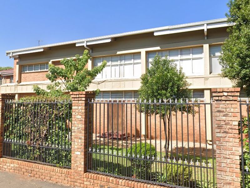 Front exterior view of the apartment building featuring a brick facade, multi-pane windows, and secure perimeter fencing.