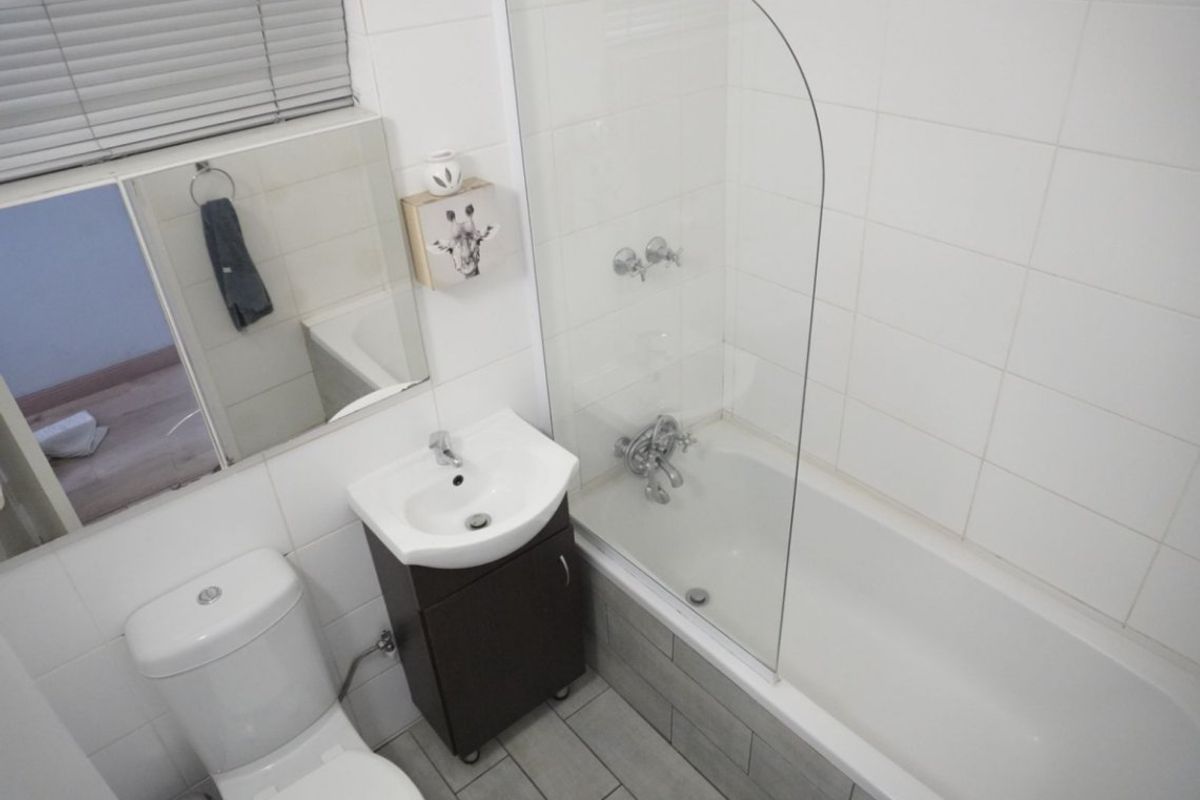 A functional bathroom featuring a bathtub with a glass shower screen, a vanity basin, and a toilet, finished with neutral wall and floor tiles.