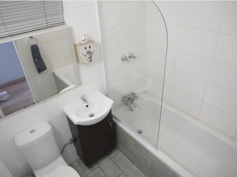 A functional bathroom featuring a bathtub with a glass shower screen, a vanity basin, and a toilet, finished with neutral wall and floor tiles.