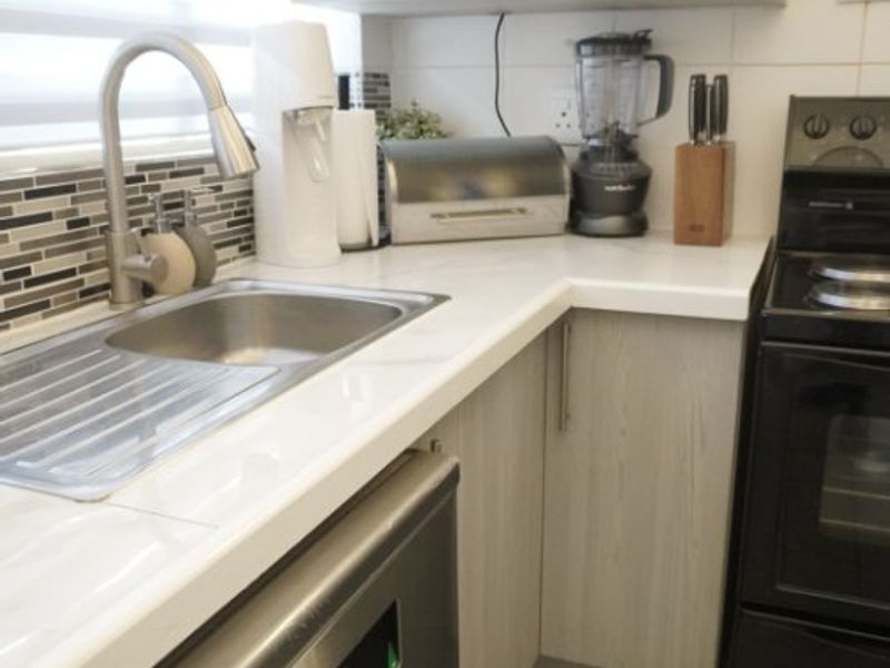A modern, well-maintained kitchen featuring stone countertops, stainless steel sink, built-in microwave, and integrated dishwasher with neutral cabinetry and tiled flooring.