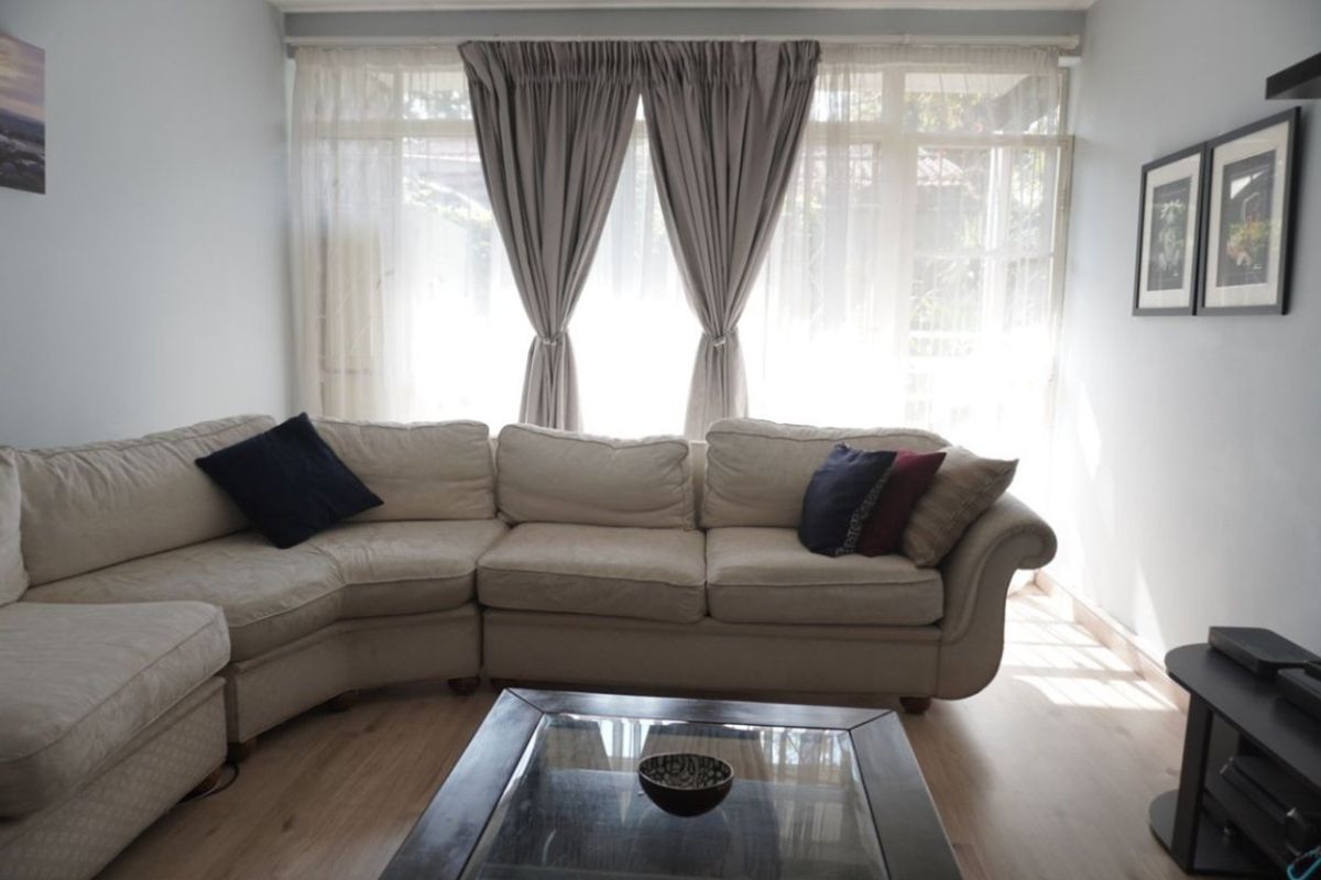 A bright living room featuring light-toned laminate flooring and a large window that allows for ample natural light.