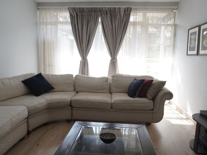 A bright living room featuring light-toned laminate flooring and a large window that allows for ample natural light.