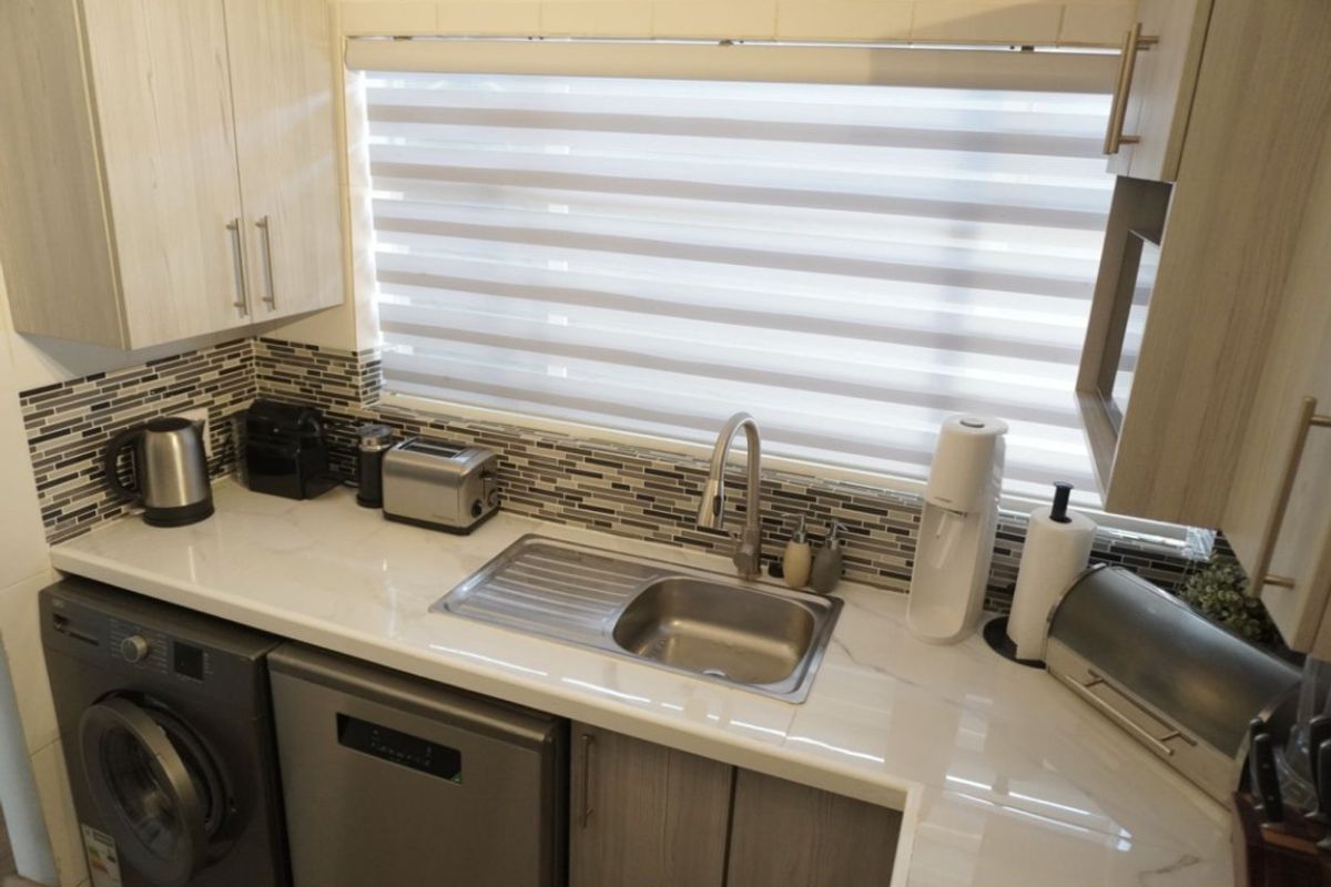A modern, well-maintained kitchen featuring stone countertops, a mosaic tile backsplash, stainless steel sink, and ample built-in cabinetry.