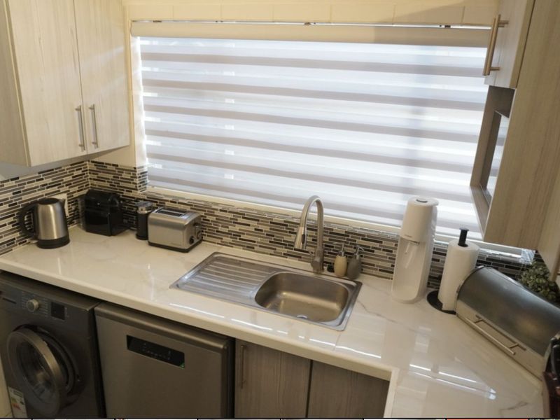 A modern, well-maintained kitchen featuring stone countertops, a mosaic tile backsplash, stainless steel sink, and ample built-in cabinetry.