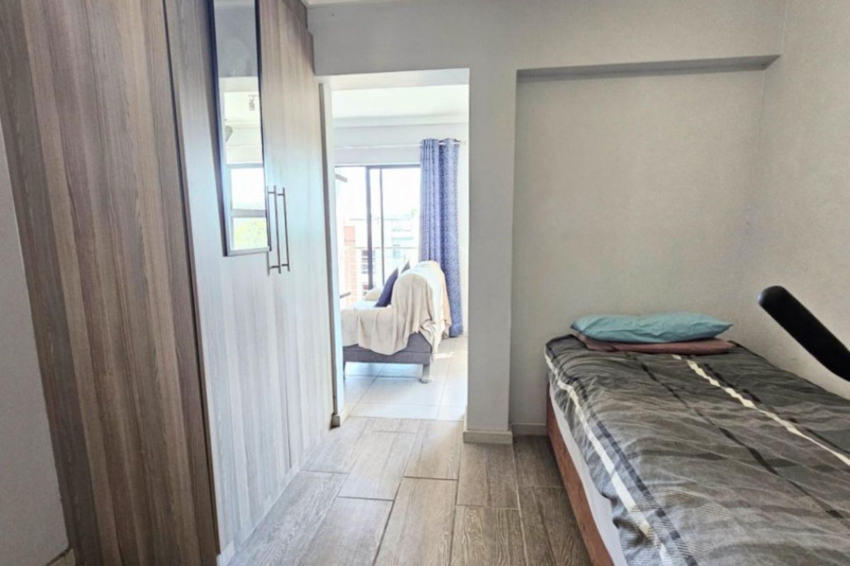 A bedroom featuring built-in wardrobes and tiled flooring, with a doorway leading to an adjacent living area.