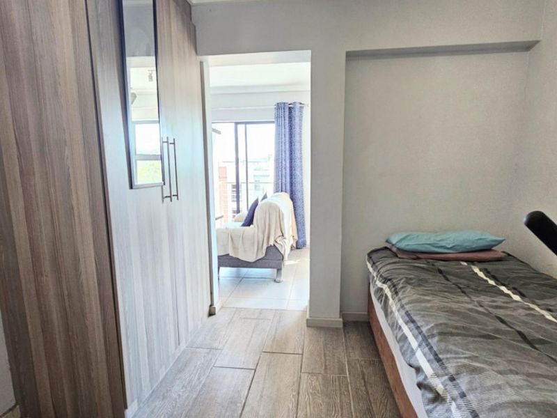 A bedroom featuring built-in wardrobes and tiled flooring, with a doorway leading to an adjacent living area.