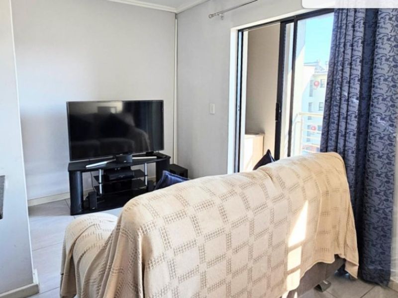 A living room area featuring tiled flooring, a floating shelf, and a sliding glass door providing access to an outdoor balcony.