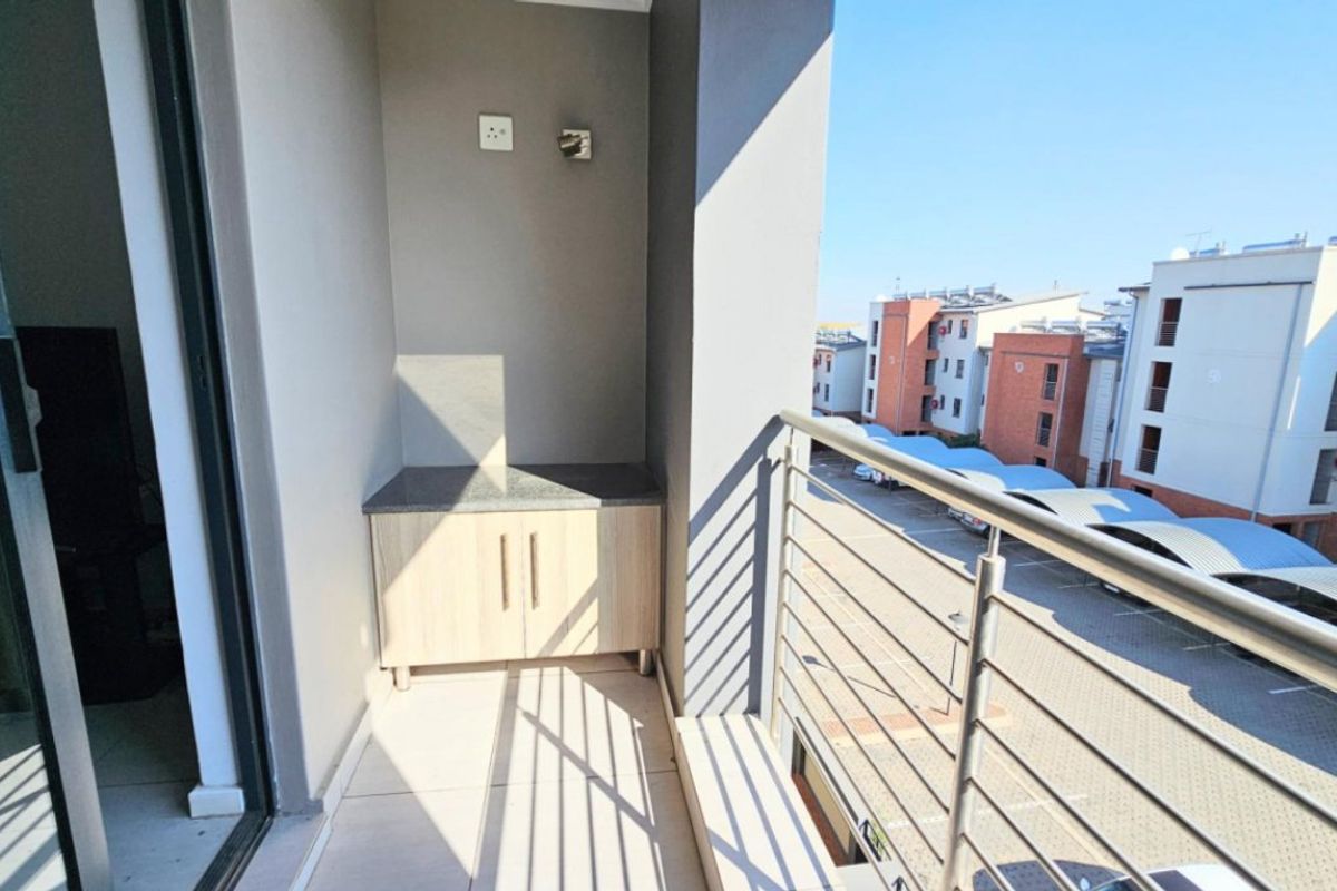 A clean, modern balcony featuring tiled flooring, a metal balustrade, and a built-in storage unit with a stone countertop.