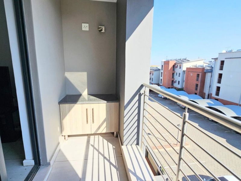 A clean, modern balcony featuring tiled flooring, a metal balustrade, and a built-in storage unit with a stone countertop.