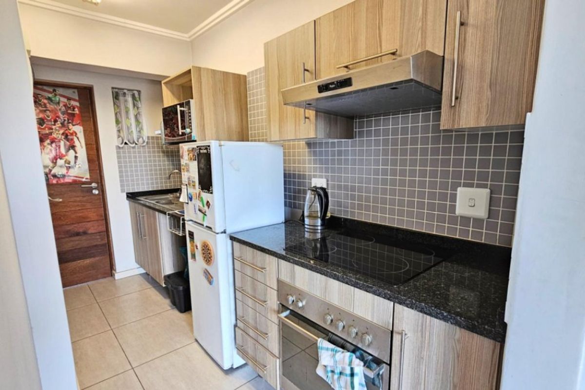 Compact kitchen featuring wood-look laminate cabinetry, granite countertops, a tiled backsplash, and integrated appliances including an electric hob, oven, and extractor fan.