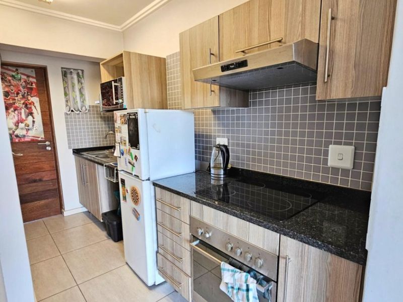 Compact kitchen featuring wood-look laminate cabinetry, granite countertops, a tiled backsplash, and integrated appliances including an electric hob, oven, and extractor fan.