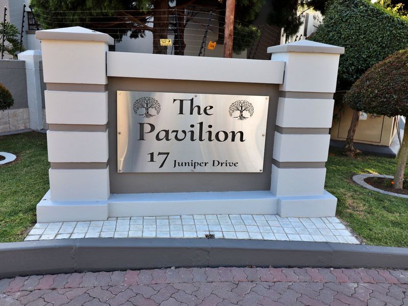 The entrance signage pillar for The Pavilion apartment complex located at 17 Juniper Drive, featuring a clean, well-maintained brick structure and metal plaque.