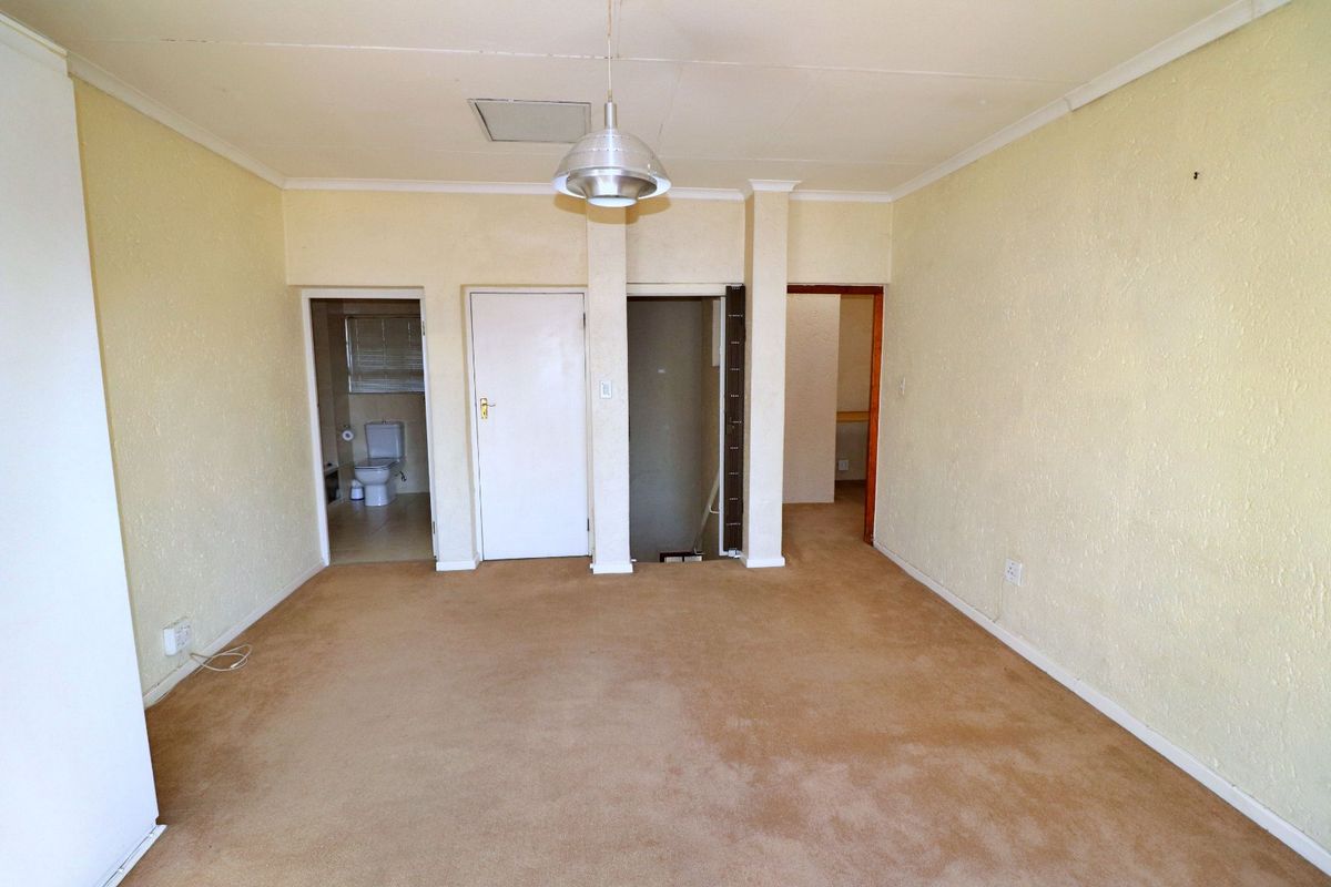 An empty living room featuring carpet flooring and a central pendant light, providing access to adjacent rooms and a bathroom.