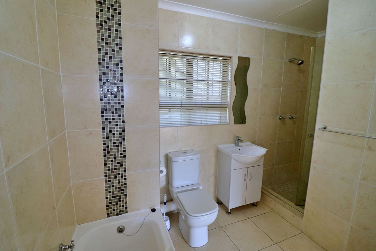 A functional bathroom featuring a shower enclosure, vanity basin, toilet, and neutral wall tiling with a decorative mosaic accent strip.
