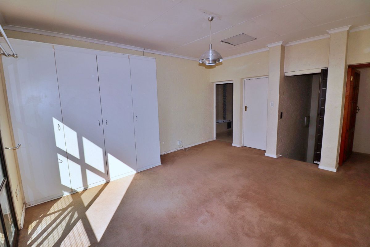 An empty bedroom featuring built-in cupboards, carpeted flooring, and a central pendant light fixture, offering a blank canvas for renovation.