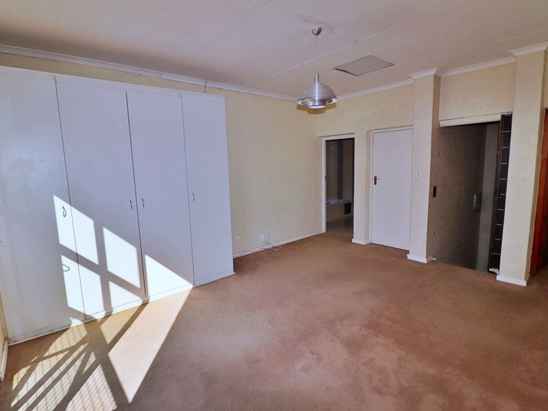 An empty bedroom featuring built-in cupboards, carpeted flooring, and a central pendant light fixture, offering a blank canvas for renovation.