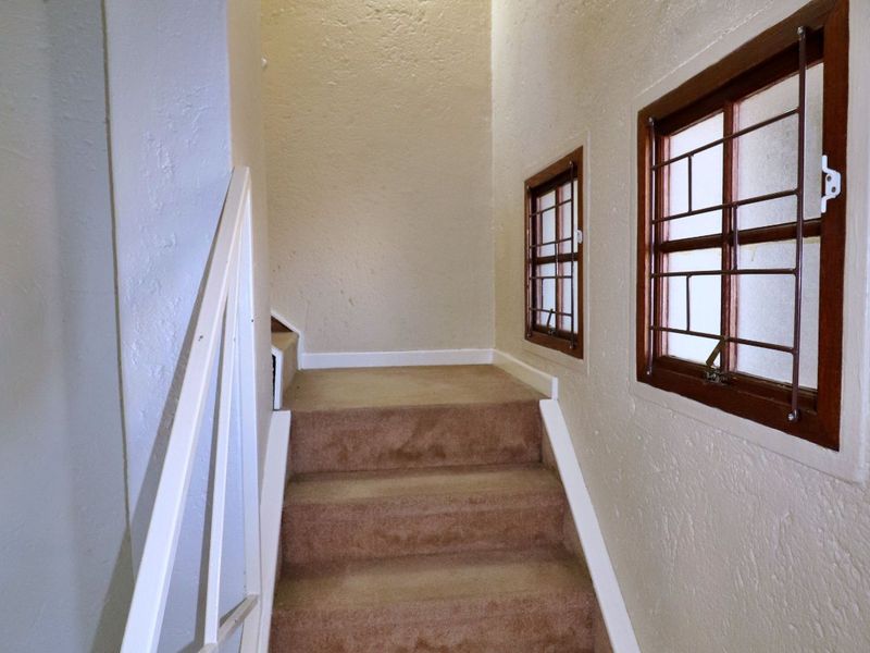 A staircase hallway featuring textured walls, timber-framed windows with security bars, and carpeted stairs.