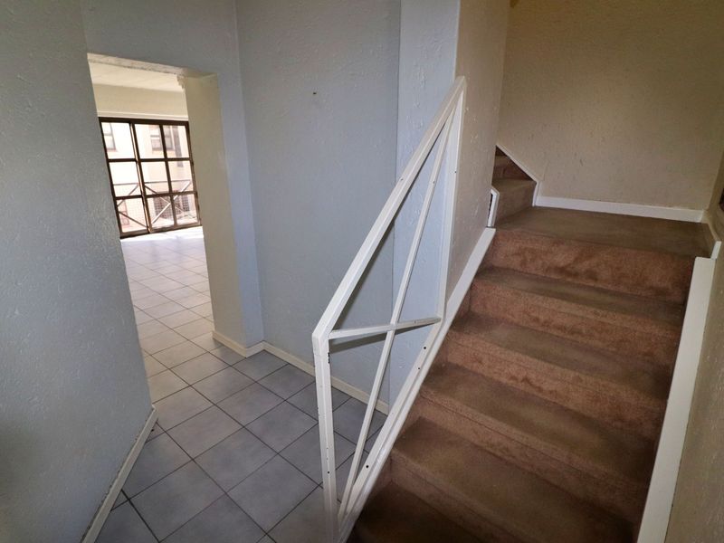 A functional hallway featuring a staircase with a metal balustrade, tiled flooring, and carpeted stairs leading to the upper level.