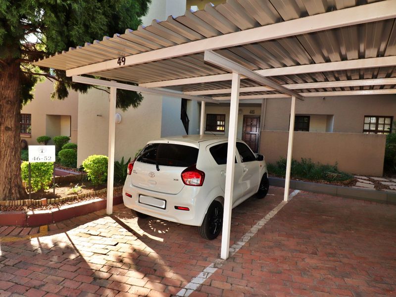 A covered carport parking bay with a corrugated metal roof and brick paved surface located within the apartment complex.