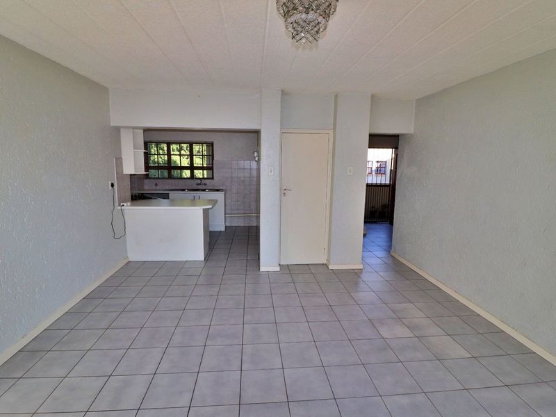 Open plan living area featuring tiled flooring, a functional kitchen with breakfast counter, and direct access to adjacent rooms.